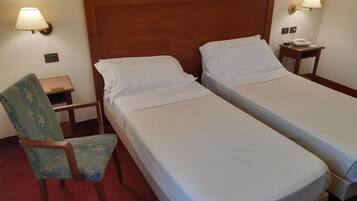A hotel room with two single beds, a wooden headboard, a chair, a nightstand, and a lamp.