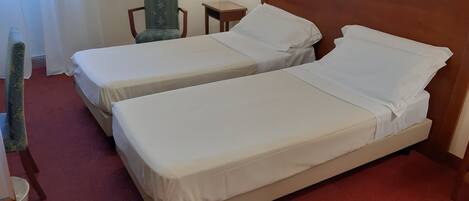 A hotel room with two single beds, a chair, a nightstand, and a lamp.