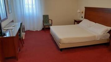A hotel room with a bed, a desk, a chair, and a nightstand.