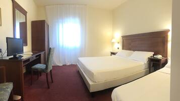 Ein Hotelzimmer mit Bett, Schreibtisch, Computer, Stuhl, Lampe und Telefon.