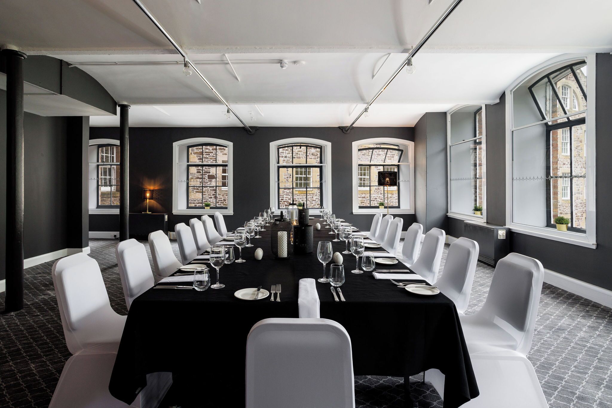 Un salón de conferencias con una larga mesa, sillas blancas y ventanas amplias con vistas a edificios.