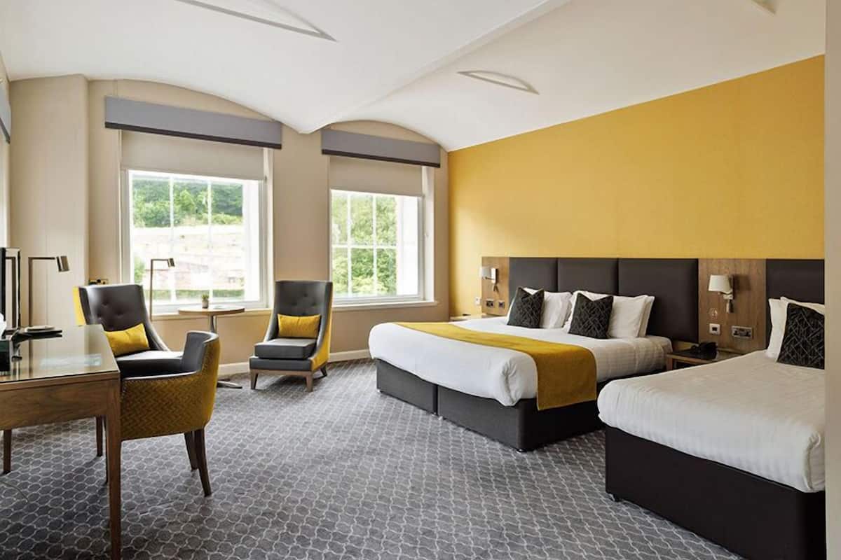 A hotel room with a large bed, two bedside tables, a desk, a chair, and two windows.