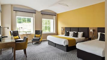 Una habitación de hotel con una cama grande, dos mesitas de noche, un escritorio, una silla y dos ventanas.