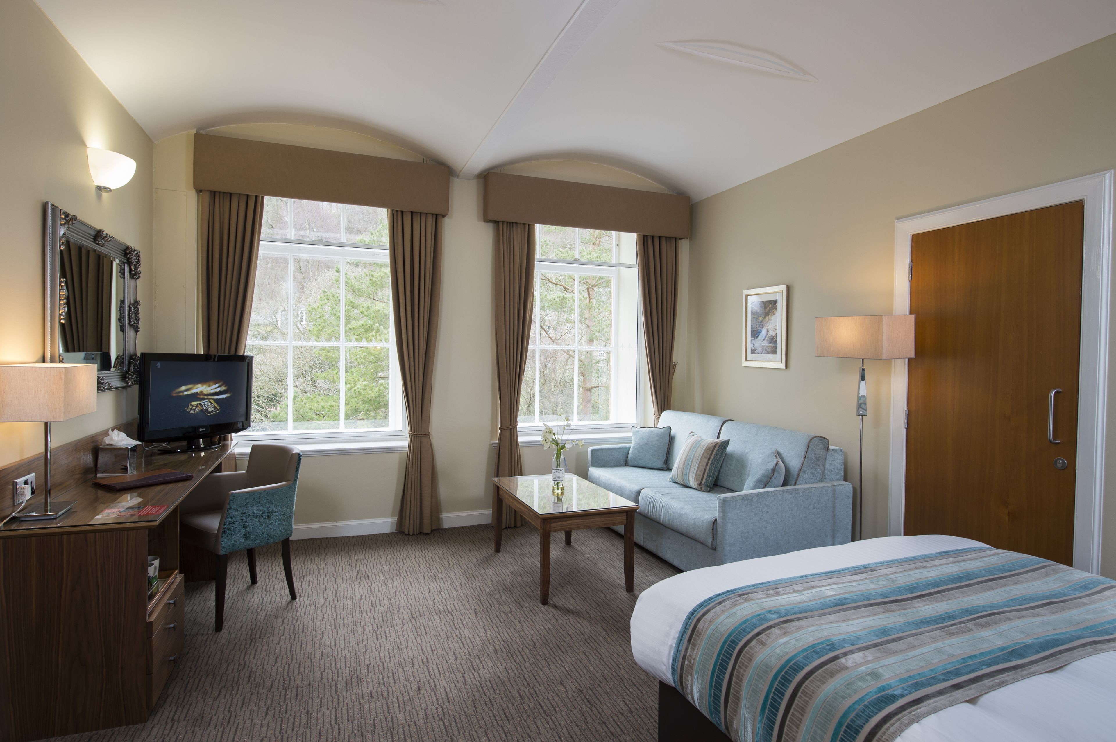 A hotel room with a bed, a desk with a computer, a sofa, and a television.