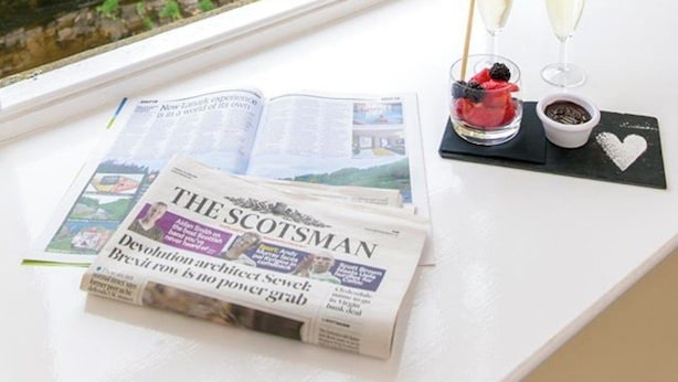A window with a newspaper, two glasses of champagne, and a heart-shaped decoration on a black coaster. - New Lanark Mill Hotel (Lanark)