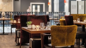 A restaurant with wooden tables, red and yellow upholstered chairs, and a bar area in the background. - New Lanark Mill Hotel (Lanark)