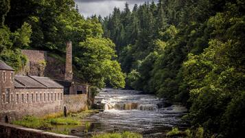 A river with a waterfall, surrounded by dense forest and a stone building with multiple windows.