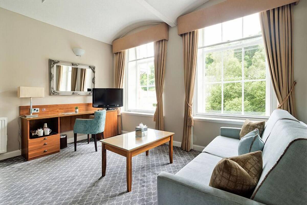 A hotel room with a sofa, a desk, a television, a mirror, and a window with curtains.
