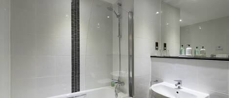Un baño moderno con ducha de vidrio, bañera blanca y lavamanos con espejo.