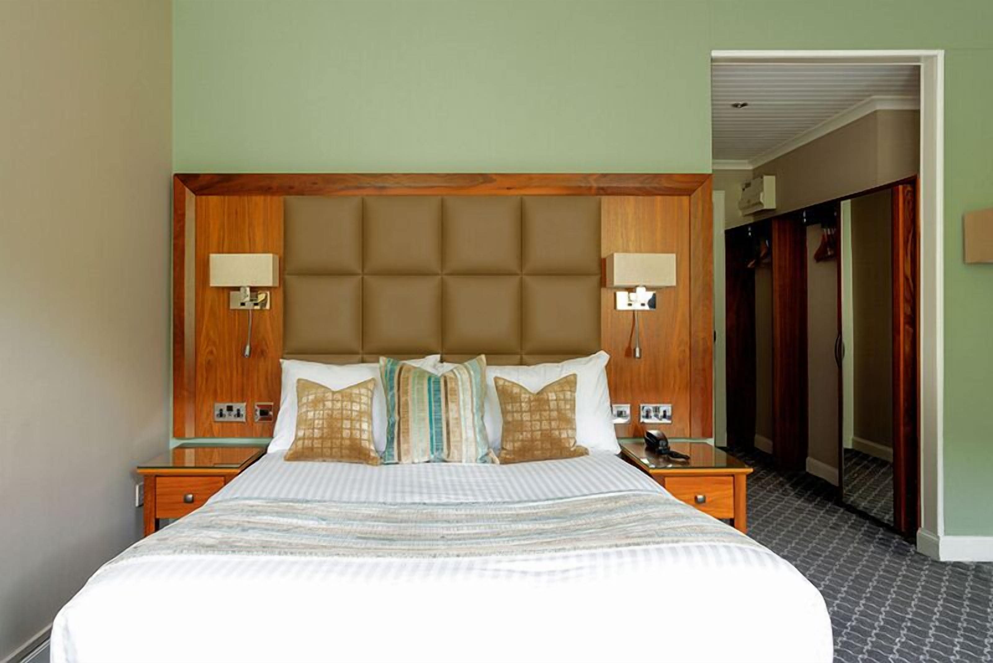 A hotel room with a large bed, wooden headboard, two bedside lamps, and a nightstand with a phone.