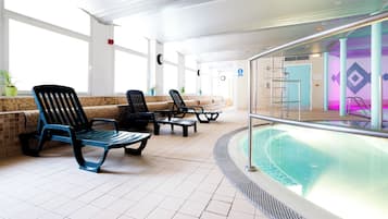 Un área de piscina con sillas de descanso, una piscina y suelo de baldosas.
