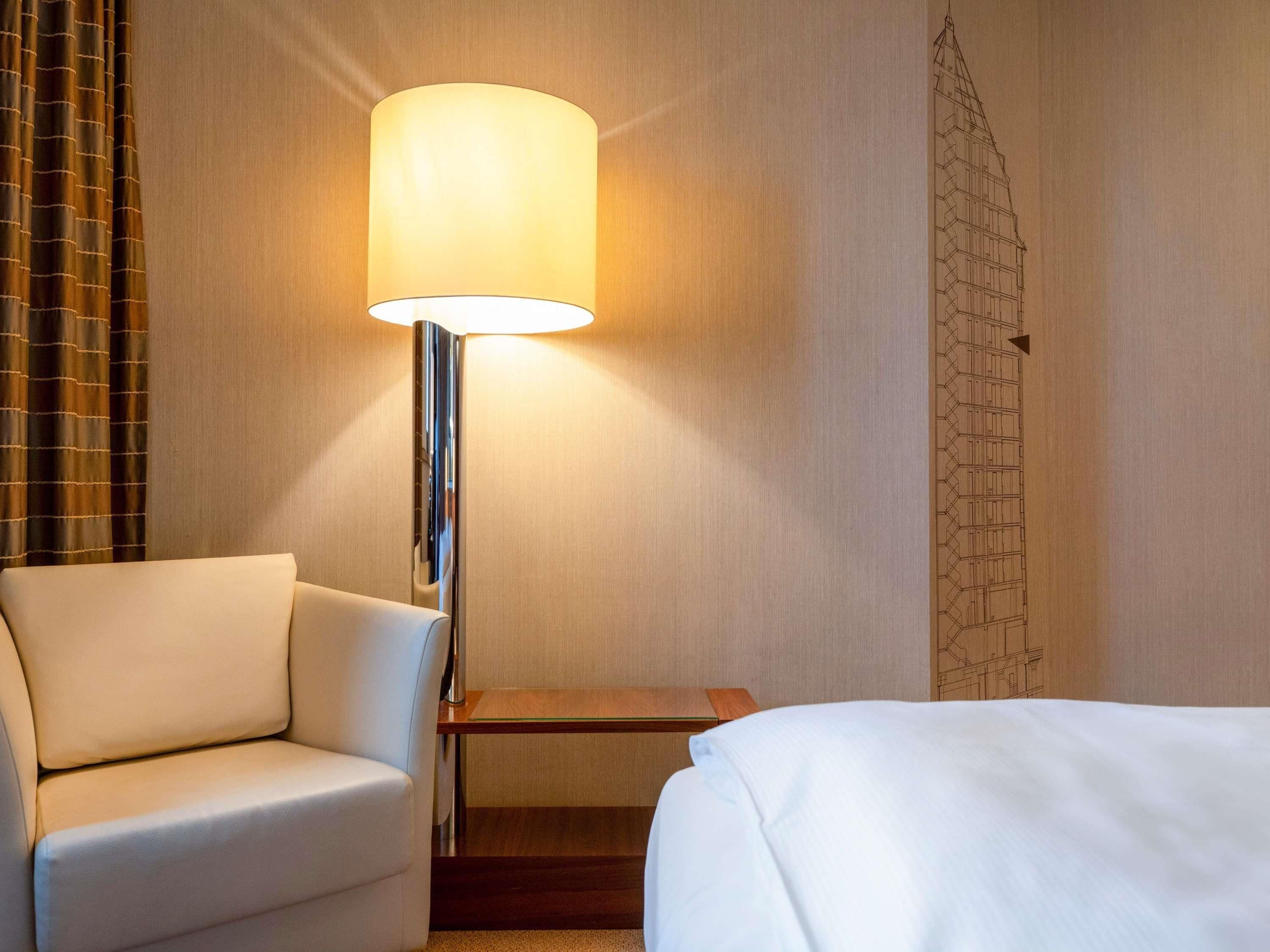 Ein Hotelzimmer mit einem Bett, einem Sessel, einem Nachttisch und einer Lampe.