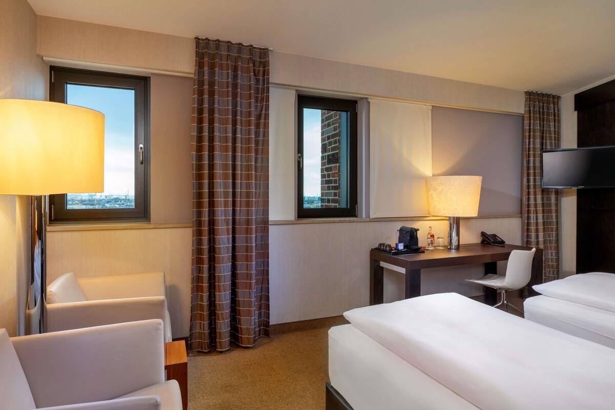 A hotel room with two beds, a desk with a telephone, a chair, a lamp, and a TV.