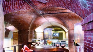 A bar area with red bar stools, a brick ceiling, and a counter with a TV screen. - Mövenpick Hotel Hamburg (Hamburg)