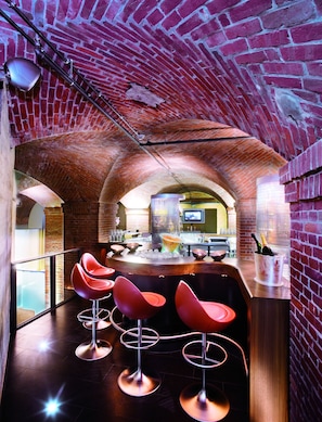 Una zona de bar con taburetes rojos, techo de ladrillo y una barra con pantalla de televisión.