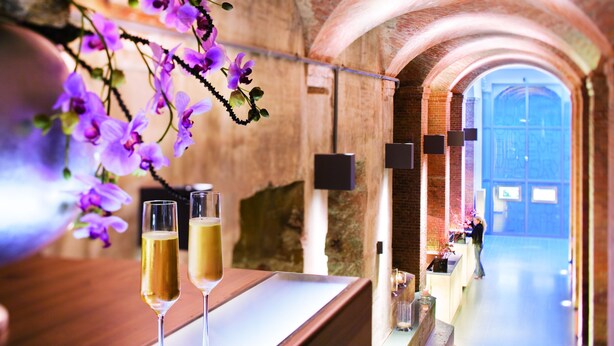 A bar area with two glasses of beer, a vase with purple flowers, and a brick ceiling. - Mövenpick Hotel Hamburg (Hamburg)