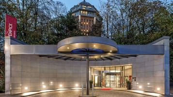 Een moderne hotelentree met een glazen gevel, een rode loper en een vlag die aangeeft dat het een Enpicck Resort is.