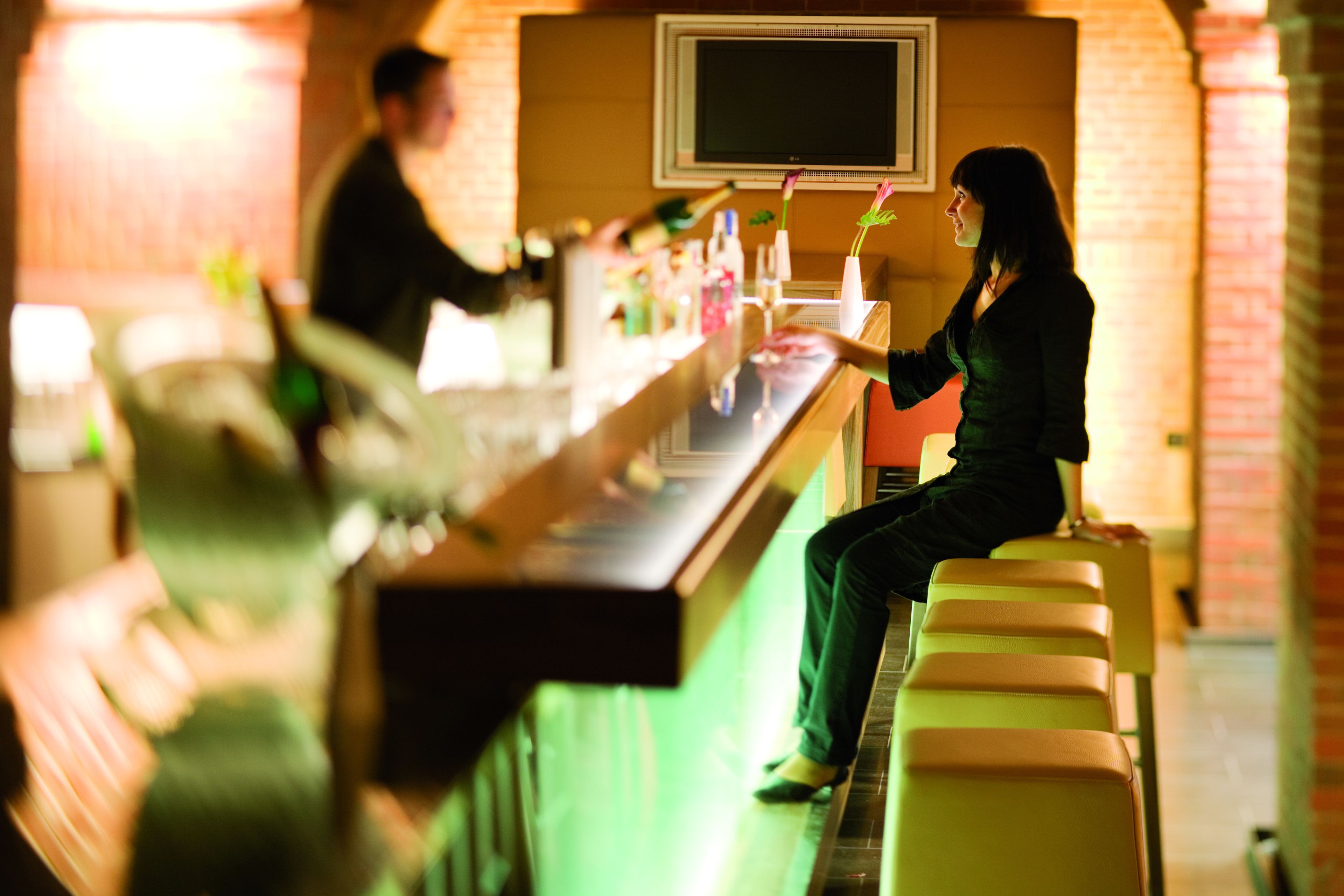 A bar area with a counter, a television mounted on the wall, and a person sitting on a bench.
