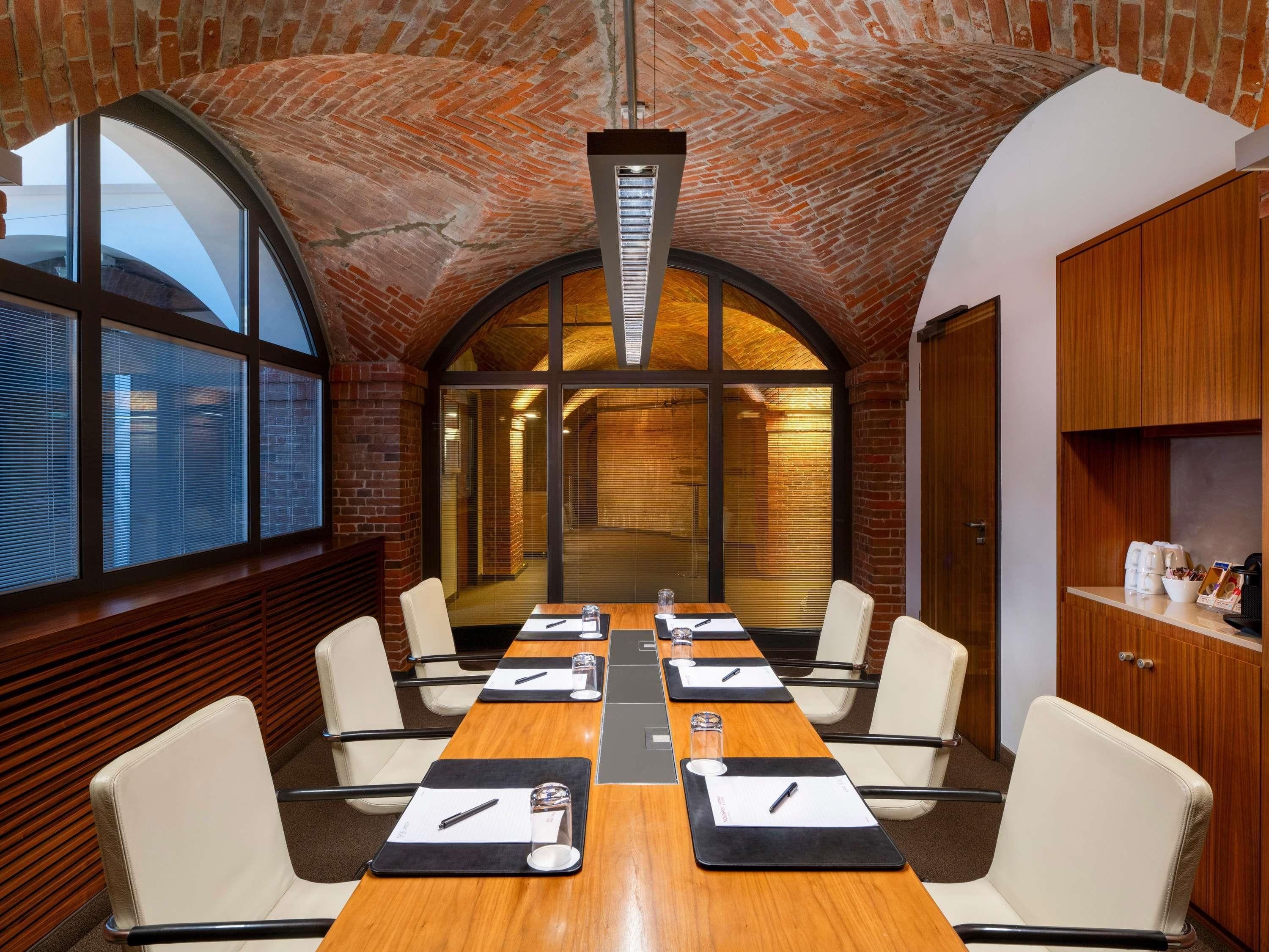 Un salón de conferencias con techo de ladrillo, ventanas amplias y una larga mesa con sillas.