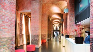 A spacious corridor with brick walls, a reception desk, and red seating areas. - Mövenpick Hotel Hamburg (Hamburg)