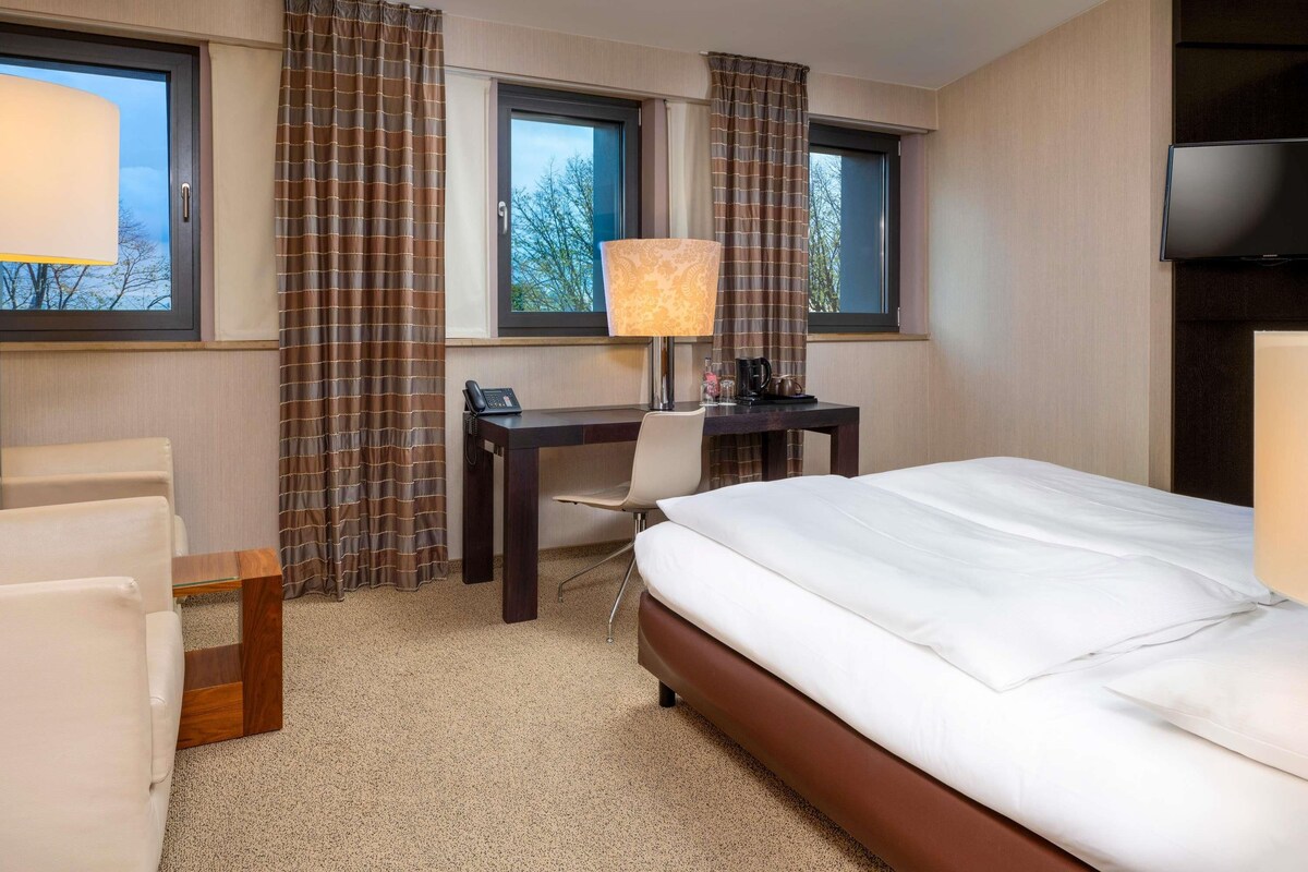 A hotel room with a bed, desk, chair, and a TV.