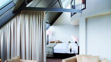 A modern hotel room with a balcony, a bed, a sofa, and a small table with a bottle.