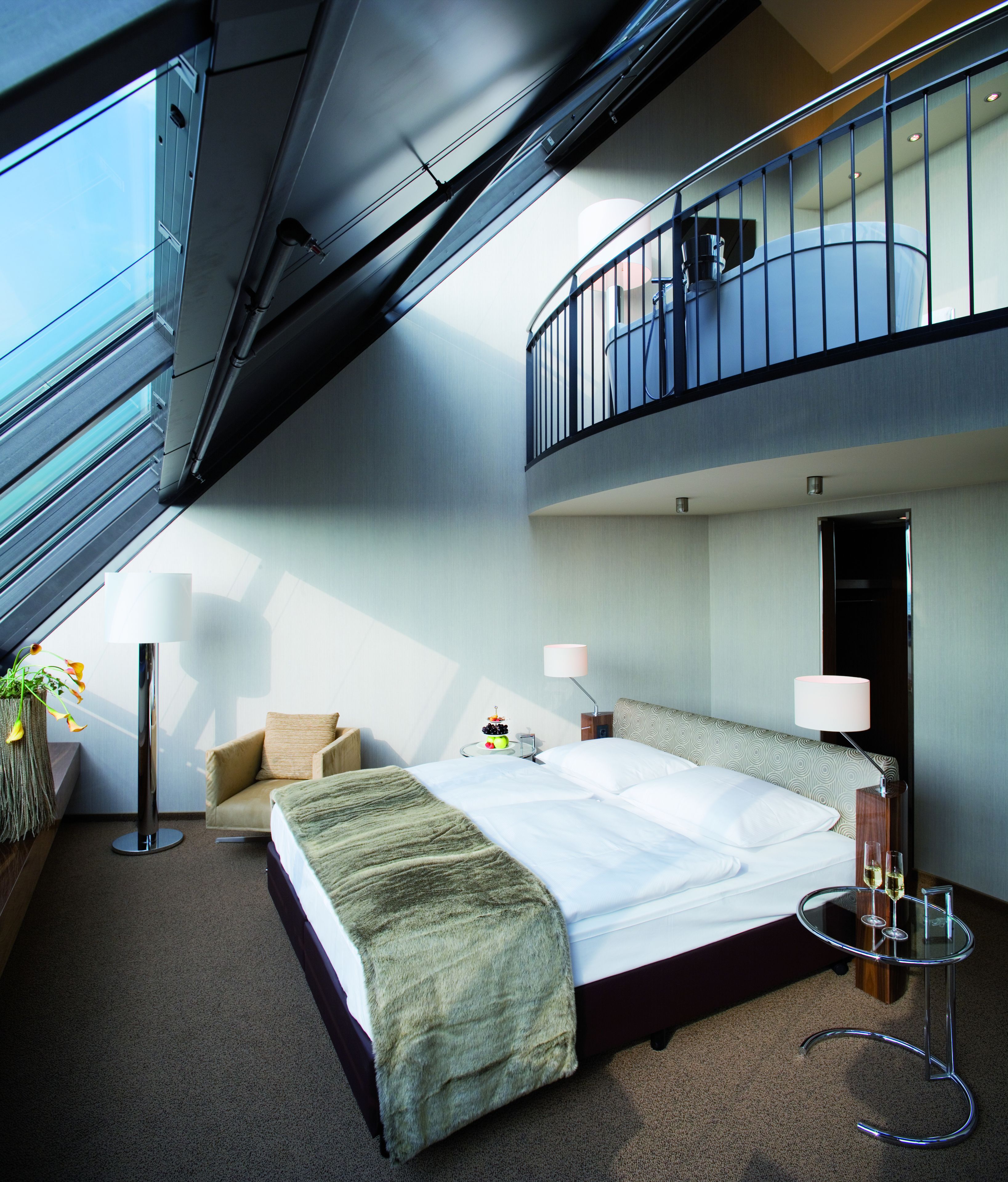 Habitación de hotel moderna con una cama grande, un balcón y vista al cielo.