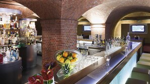A bar area with brick arches, shelves of liquor bottles, a fruit bowl, and bar stools. - Mövenpick Hotel Hamburg (Hamburg)