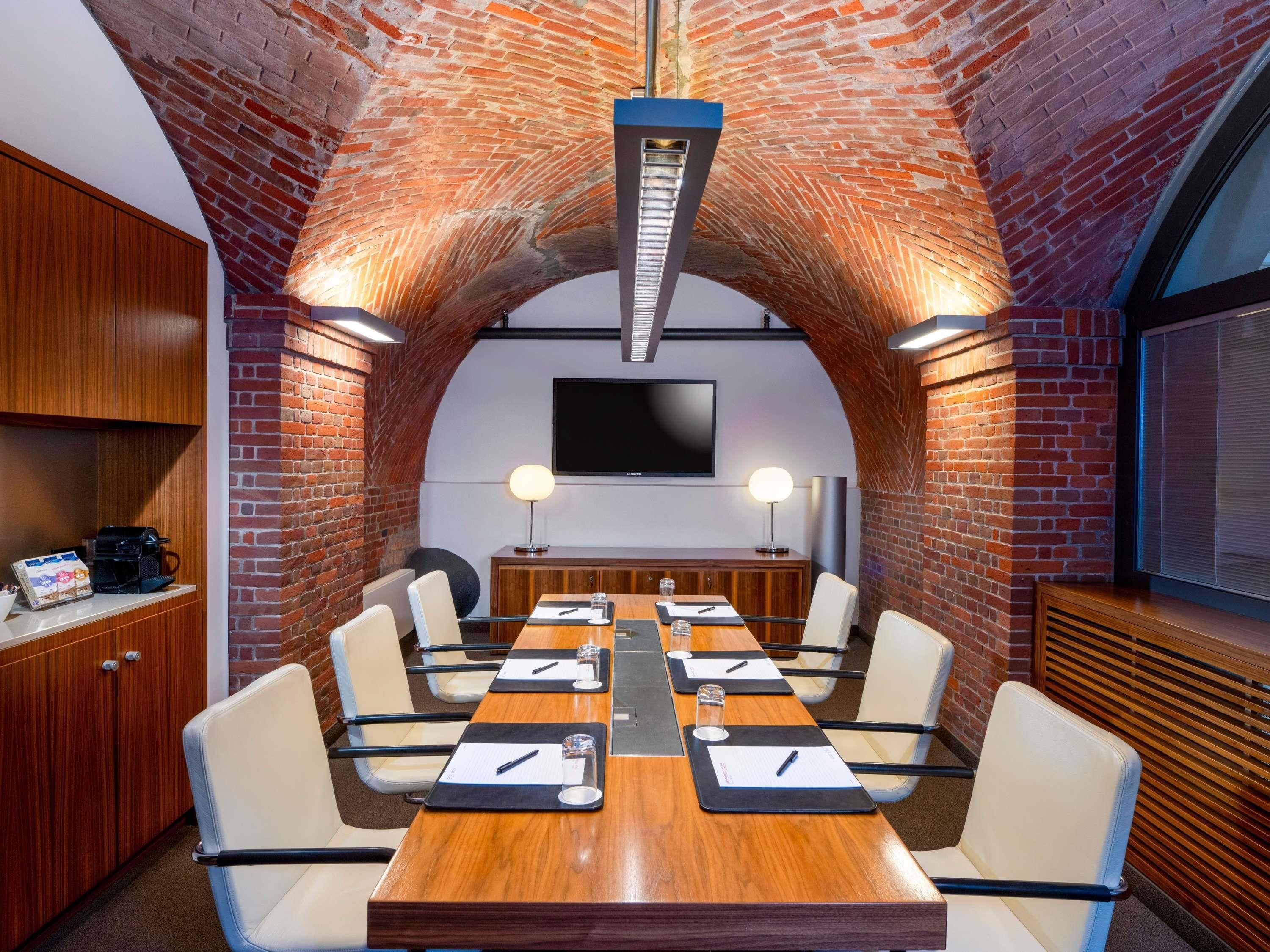 A conference room with a long table, chairs, a TV, and a brick wall.