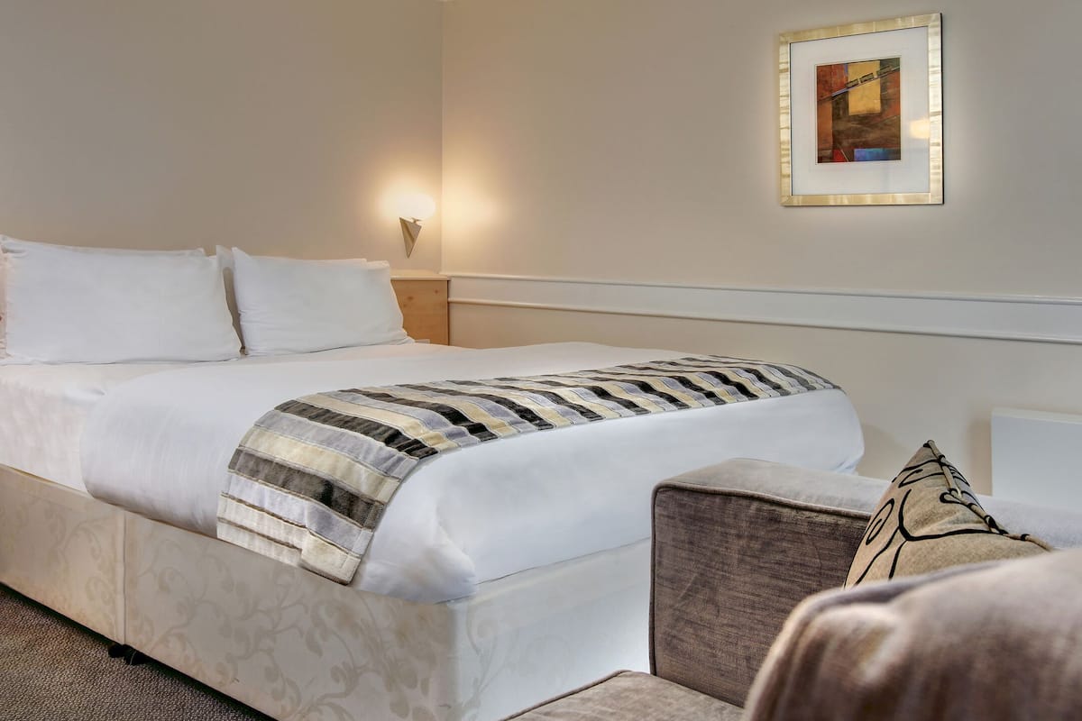 Habitación de hotel con cama, mesita de noche con teléfono, sillón y un cuadro en la pared.