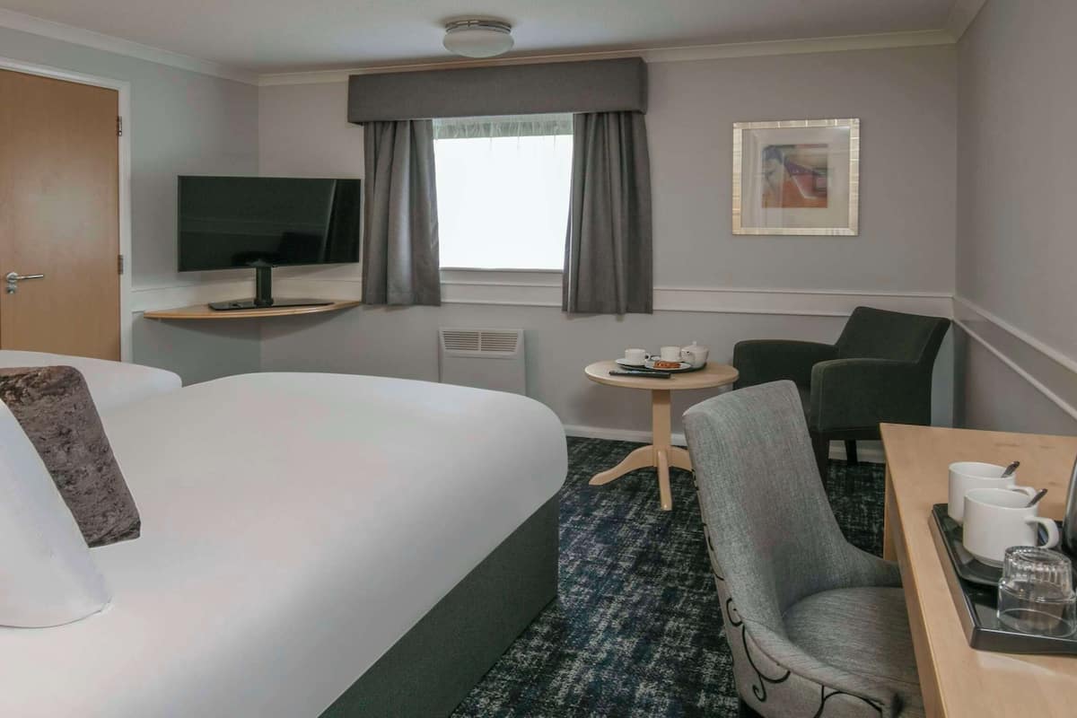 Habitación de hotel con una cama grande, un escritorio con silla, un televisor y una mesita con tazas y una tetera.