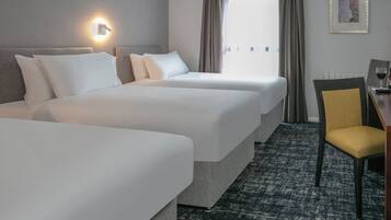 Habitación de hotel con dos camas, un escritorio con silla, una lámpara de pared y un ventanal con cortinas.