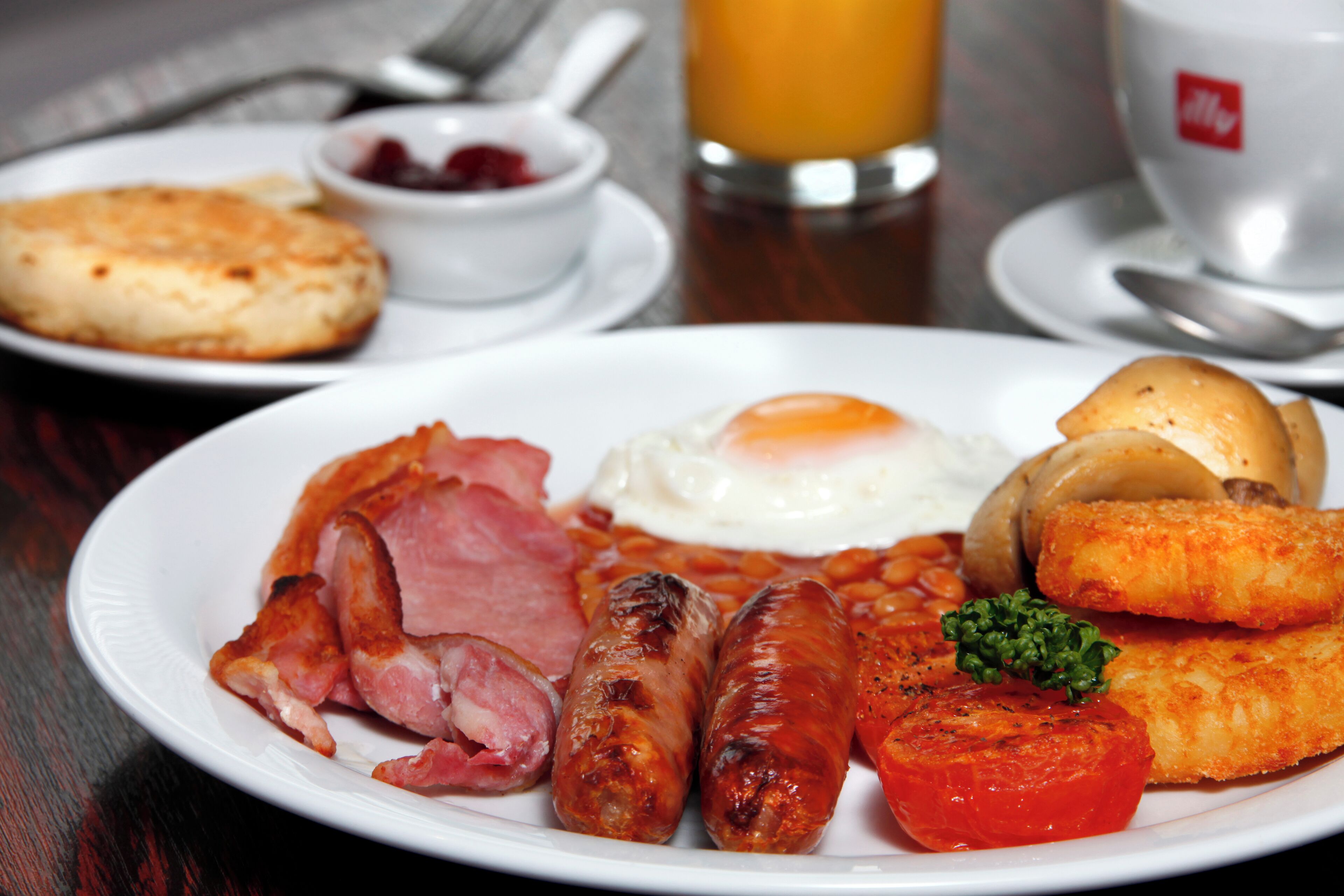 Une assiette de petit-déjeuner comprenant des œufs, des saucisses, des tomates et du jambon.