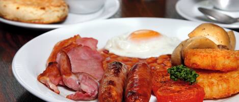 Une assiette de petit-déjeuner comprenant des œufs, des saucisses, des tomates et du jambon.