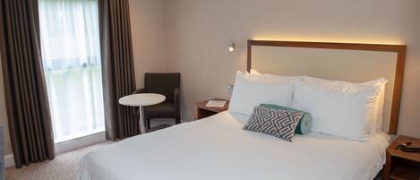 Habitación de hotel con una cama grande, una mesa redonda pequeña, una silla y vistas al exterior a través de la ventana.