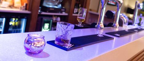 A bar area with a glass and a candle on the counter, a coffee machine, and multiple taps.