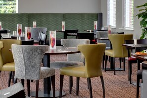 Un restaurant avec un mur orné d’un motif végétal, de nombreuses tables et chaises, et un sol en briques.