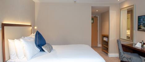 A hotel room with a large bed, a desk, a chair, and a mirror.
