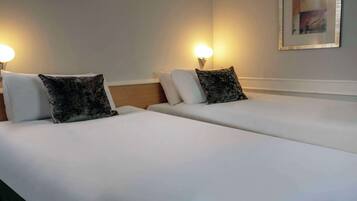 Two single beds with white linens and dark patterned pillows, each with a wall-mounted night light.