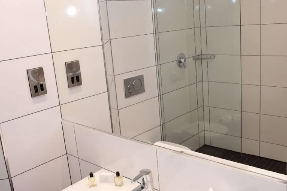 Een moderne badkamer met witte tegels, een douchecabine van glas en een zichtbare kraan.