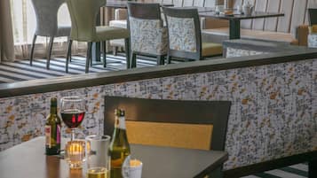 Un restaurante con barra, asientos con tapicería estampada y una mesa con copas y botellas de vino.
