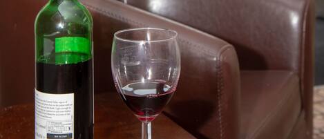 Una botella de vino y un vaso vacío sobre una mesa en una habitación con un sofá de cuero y vistas a un edificio de ladrillo a través de una ventana.
