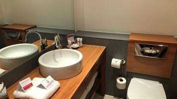 Une salle de bain moderne avec un double lavabo, un miroir, des toilettes et une petite étagère contenant des articles de toilette.