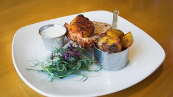 A plate with roasted chicken, potatoes, a small bowl of sauce, and a side salad.