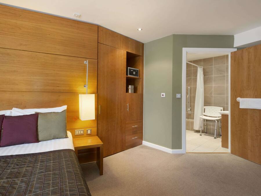 Una camera d'albergo con un letto, un comodino, un armadio in legno e un bagno visibile attraverso una porta aperta.