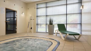 A spa area with a hot tub, a green lounge chair, and a large window with blinds. - Ramada Plaza by WyndhamWrexham (Wrexham)