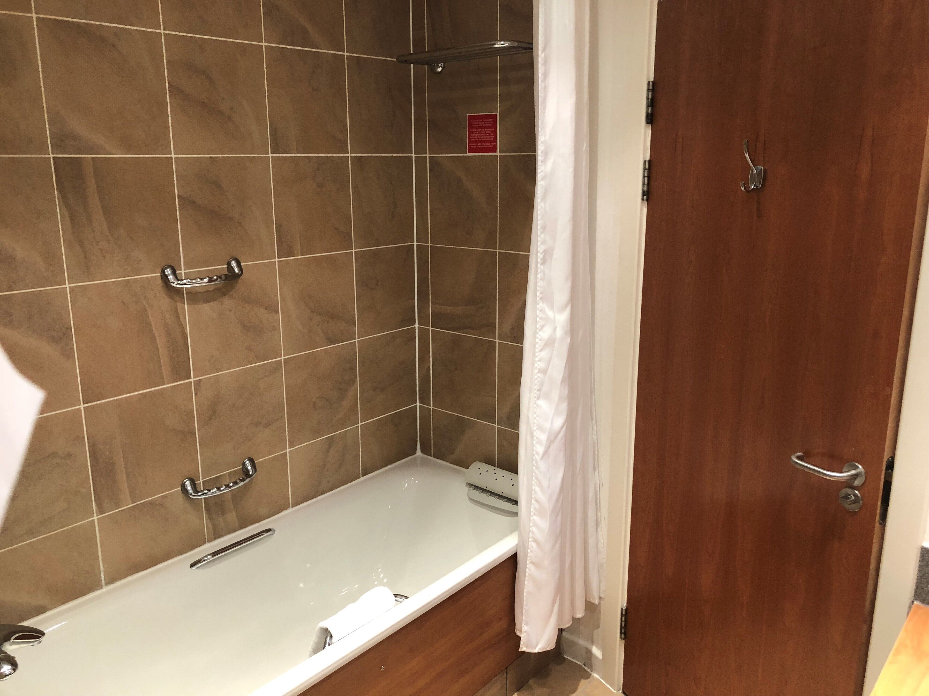 A bathroom with a bathtub, a shower area, and a wooden door.