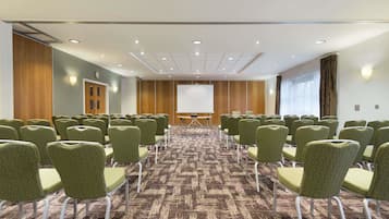Una sala conferenze con file di sedie verdi, una lavagna e un pavimento rivestito di moquette.