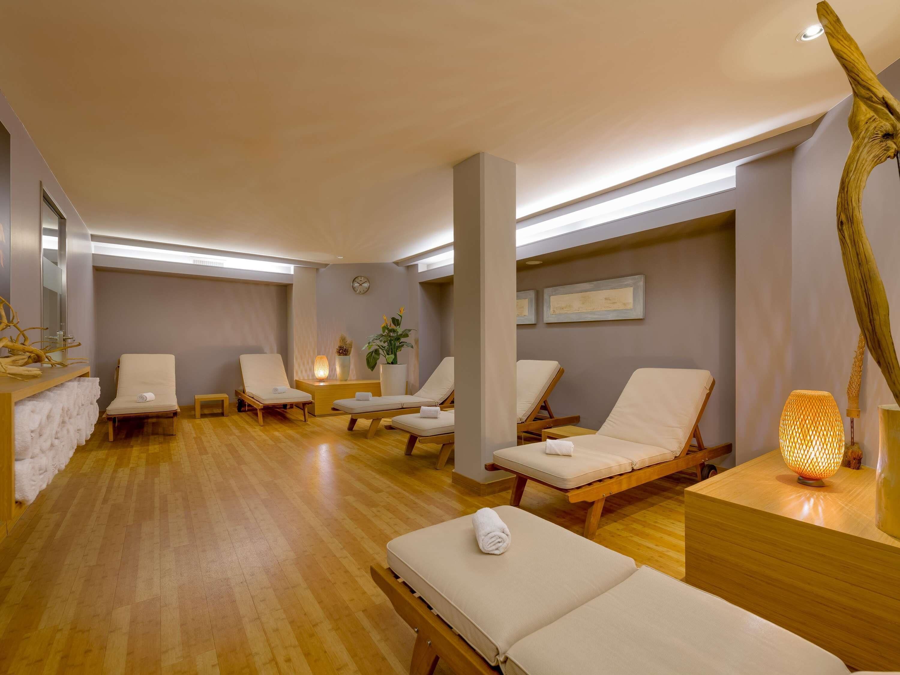 A spa room with wooden floors, multiple lounge chairs, a reception desk, and a wall clock.