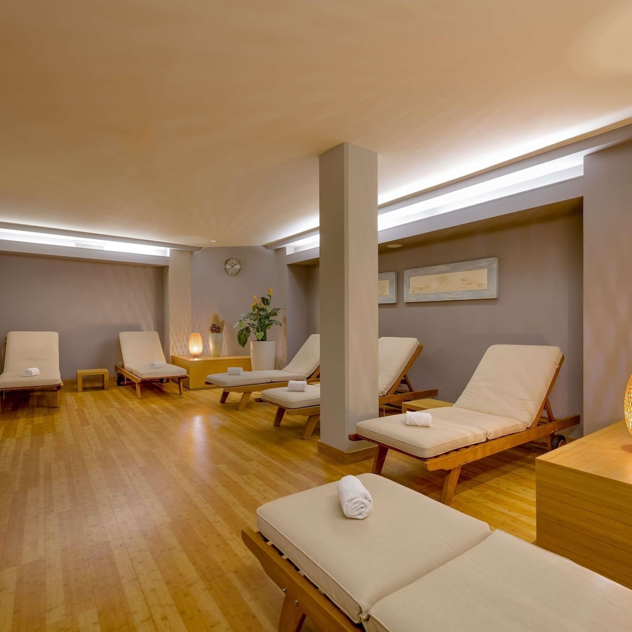 A spa room with wooden floors, multiple lounge chairs, a reception desk, and a wall clock.